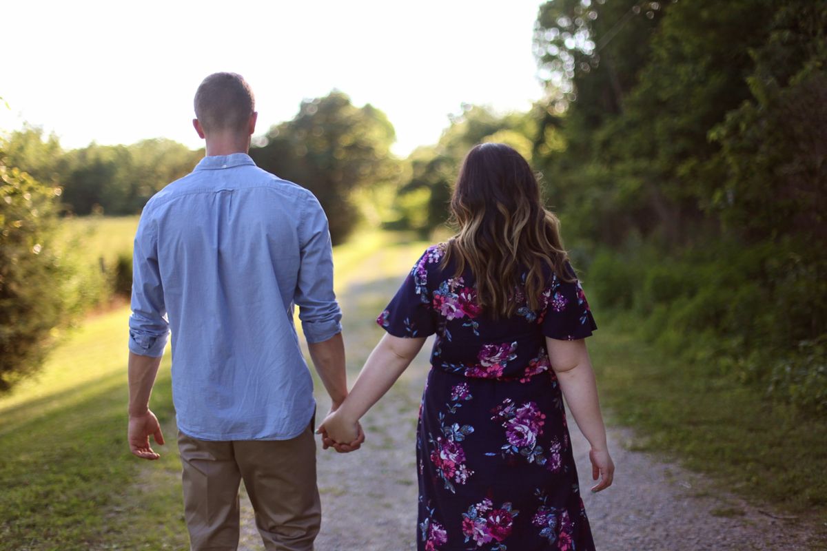A couple walking away from the camera on a country path, holding hands